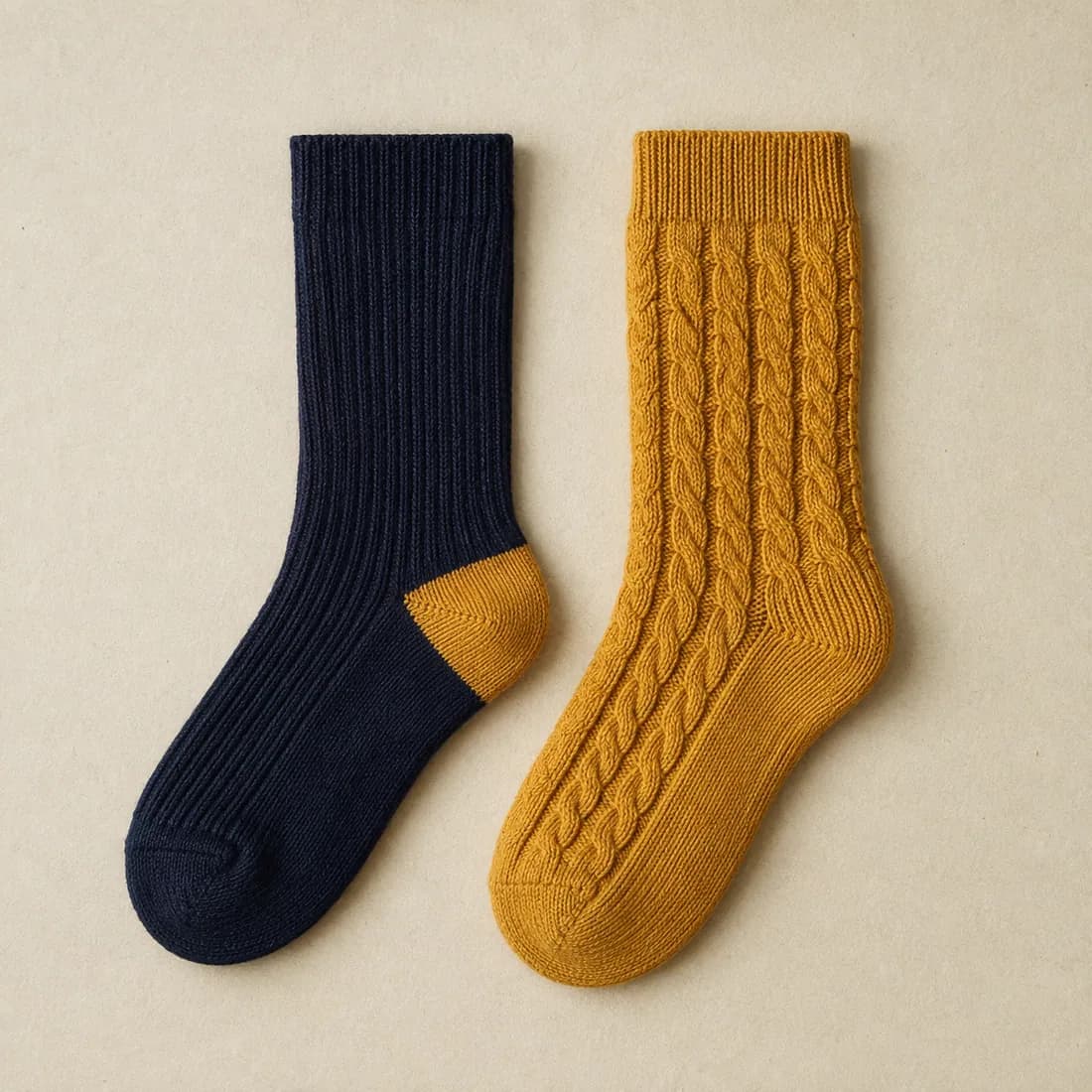 A navy ribbed sock with a mustard heel laid flat beside a mustard cable knit sock of the same length