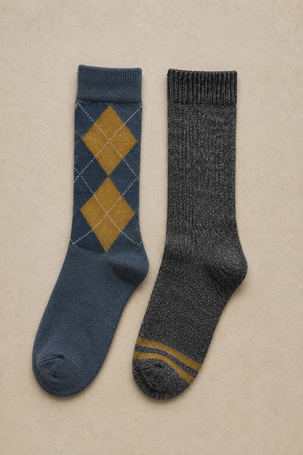 A slate argyle sock with mustard diamonds laid flat beside a charcoal marl sock with mustard toe stripes
