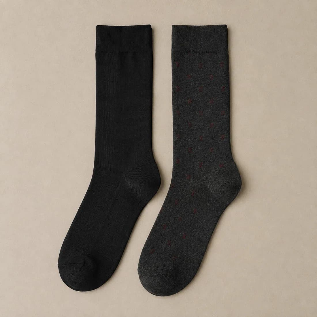 A black fine gauge dress sock laid flat beside a charcoal fine gauge dress sock with a small burgundy motif