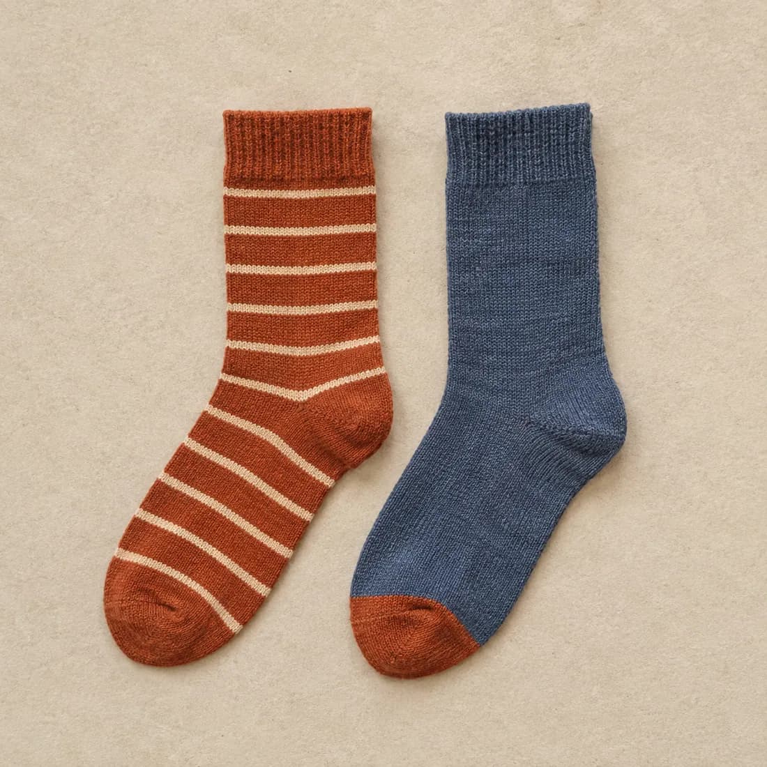 A rust sock with thin cream stripes laid flat beside a slate sock with a rust toe