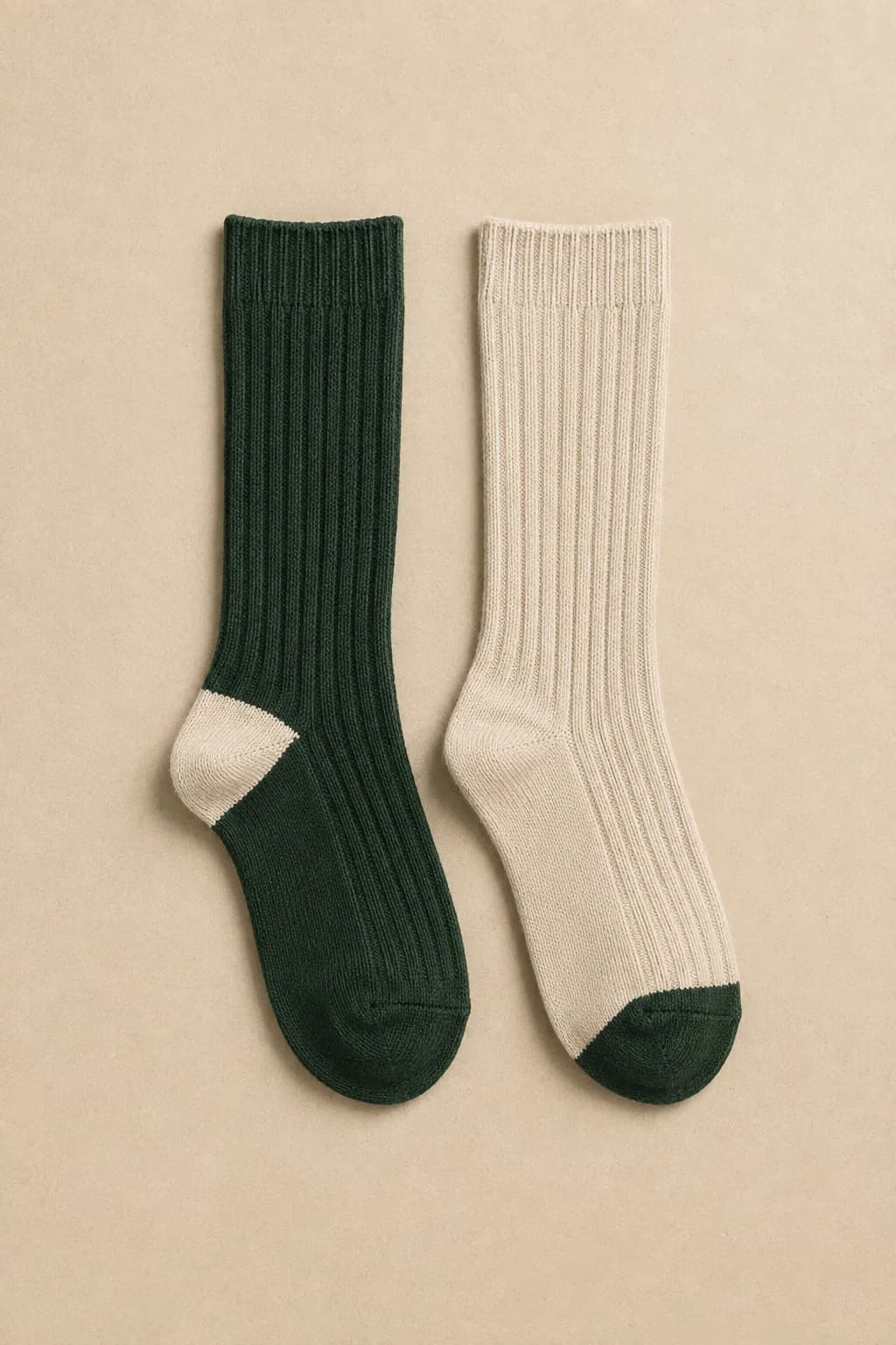 A forest green ribbed sock with a cream heel laid flat beside an oatmeal ribbed sock with a forest green toe