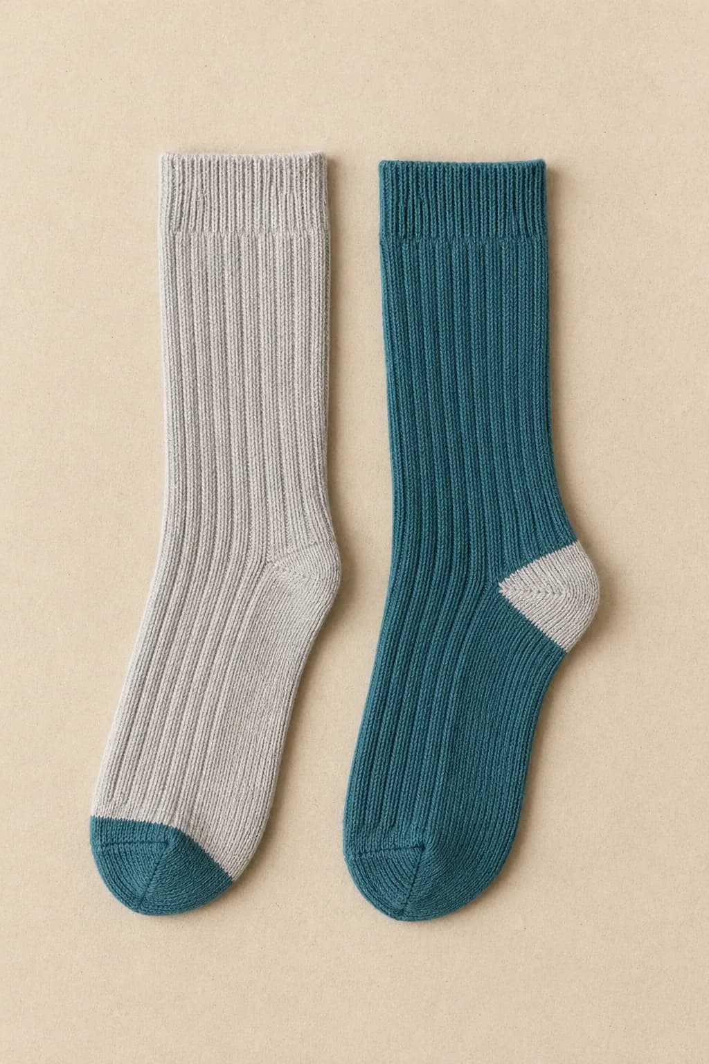 A pale grey ribbed sock with a teal toe laid flat beside a teal ribbed sock with a pale grey heel