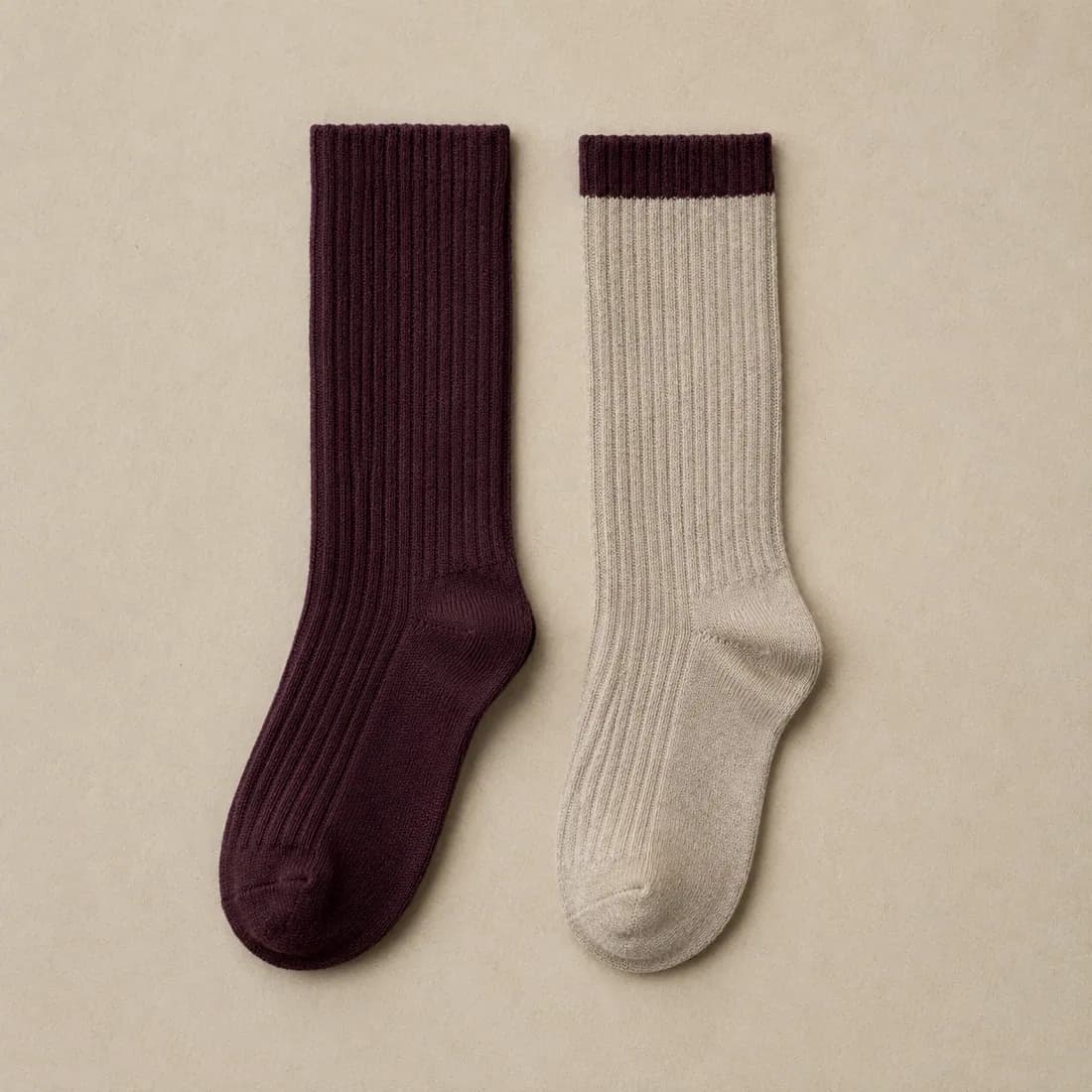 A plum ribbed sock laid flat beside an oatmeal sock with a plum cuff band
